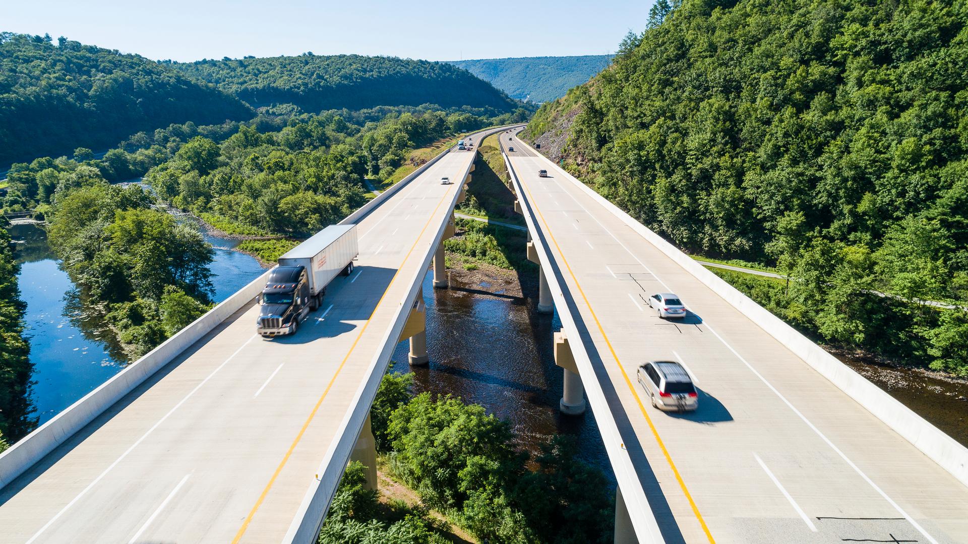Vehicles travel on a scenic roadway in Pennsylvania that bridges over a winding river.