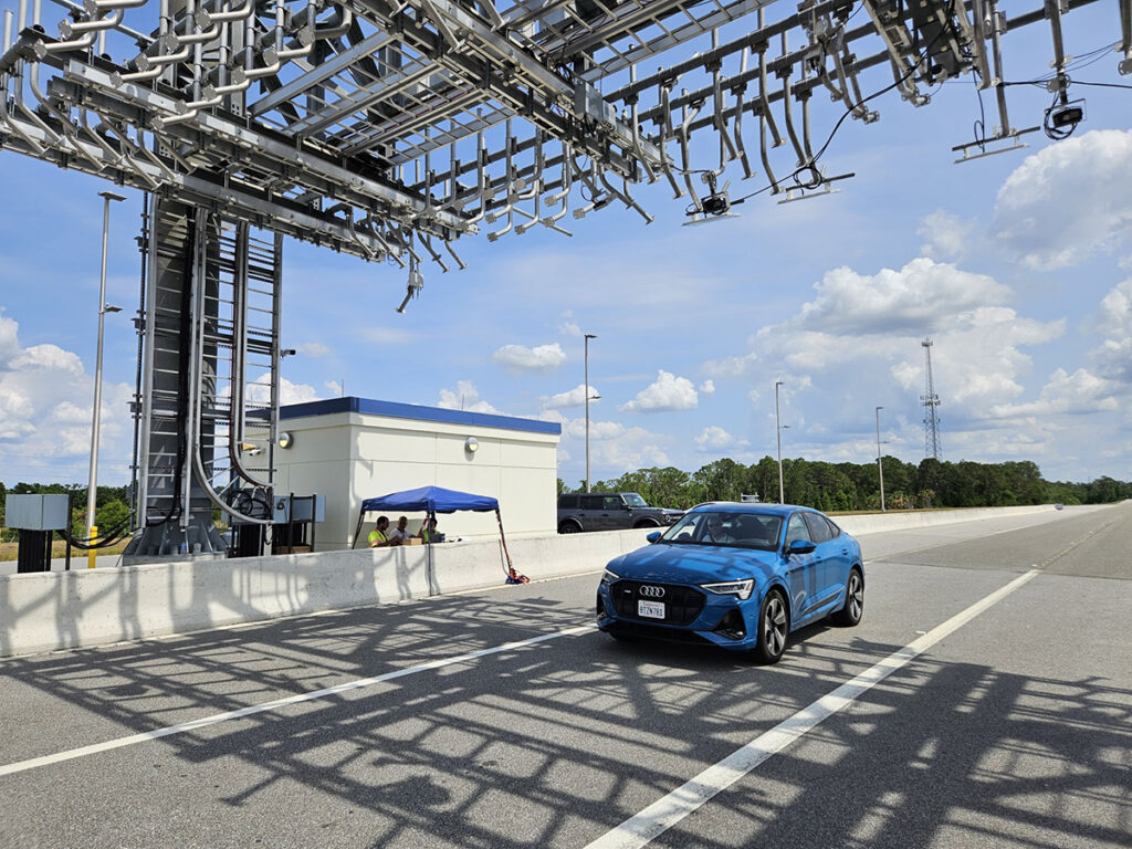 A blue car tests out the C-V2X technology, passing under a metal tolling structure.