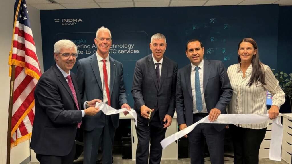 Indra Group USA executives smile and cut a large white ribbon at their new facility.